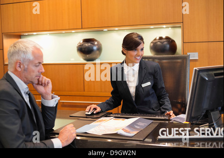 Receptionist working on a desktop pc with a businessman at the hotel reception counter Stock Photo