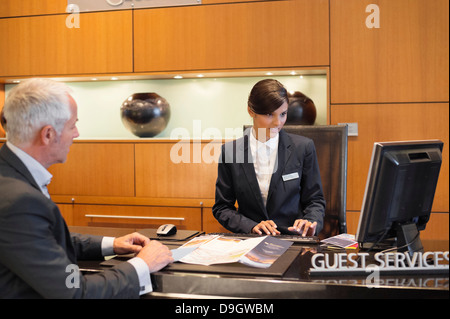 Receptionist working on a desktop pc with a businessman at the hotel reception counter Stock Photo