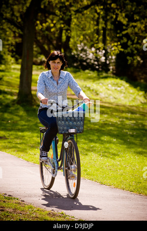 Young casually dressed caucasian woman riding a bike in a UK park Stock Photo
