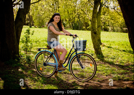 Young casually dressed caucasian woman on a traditional bike, stationary, under a tree, in a UK park. Stock Photo