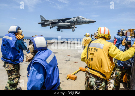 US Navy sailors on amphibious assault ship USS Bonhomme Richard shield their faces from jet exhaust as an AV-8B Harrier jet aircraft lands on the ship's flight deck June 19, 2013 operating in the East China Sea. Stock Photo