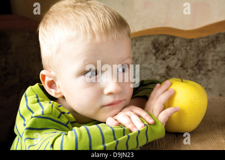 Child dreaming and thinking at home with yellow apple, close up portrait with copy space. Stock Photo