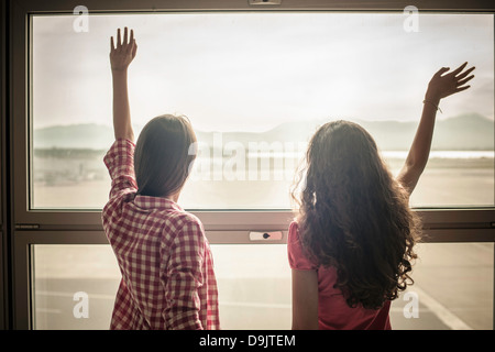 Two teenage girls waving through window