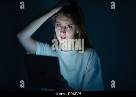 A young woman using a tablet computer iPad looking worried anxious concerned victim cyber bullying bullied on-line Stock Photo