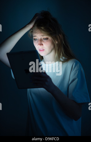 A young woman using tablet computer iPad looking worried anxious concerned scared frightened sad upset tearful depressed bullied Stock Photo