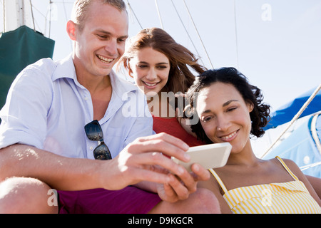 Three young friends on yacht using smartphone Stock Photo