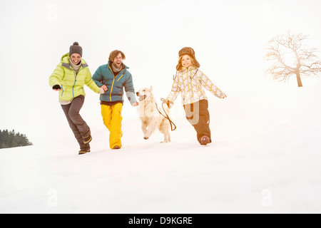 Family running on snow with dog