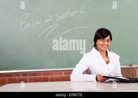 young beautiful school teacher sitting in front of blackboard Stock Photo