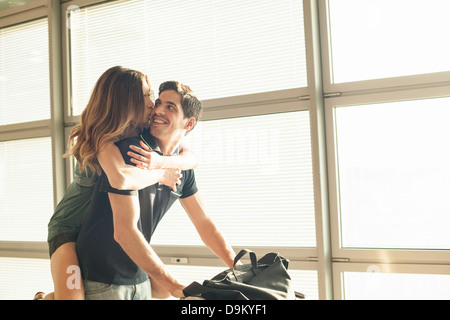 Young man giving woman piggy back in airport Stock Photo