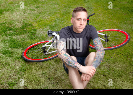 Portrait of young tattooed man sitting on grass Stock Photo