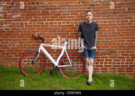 Young tattooed man leaning against brick wall Stock Photo