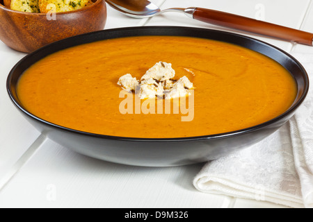 Pumpkin Soup roast pumpkin soup topped with feta cheese and cumin seeds, in a black bowl on a white background. Stock Photo