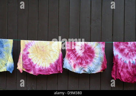 shirts t-shirts tee shirt clothsline rope hanging hang dry colors colored tie dye tie-dye brown wood wall Stock Photo