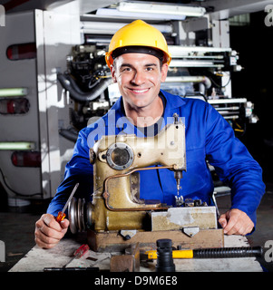 happy mechanic repairing industrial sewing machine in factory Stock Photo