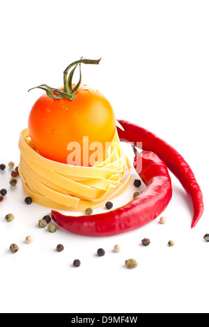 Orange tomato in a raw pasta nest with red chili peppers Stock Photo