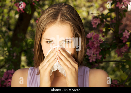 Young woman with allergy during sunny day is wiping her nose. Stock Photo