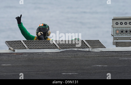 A US Navy Aviation Boatswain’s Mate gives the go signal during flight operations on the flight deck of the aircraft carrier USS Nimitz June 13, 2013 in the Gulf of Oman. Stock Photo