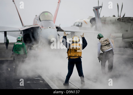 A US Navy Aviation Boatswain’s Mate directs an F/A-18C Hornet fighter aircraft to a catapult on the flight deck of the aircraft carrier USS Carl Vinson June 11, 2013 off the coast of Southern California. Stock Photo