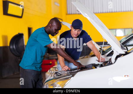 African man showing auto mechanic his car problem inside workshop Stock Photo