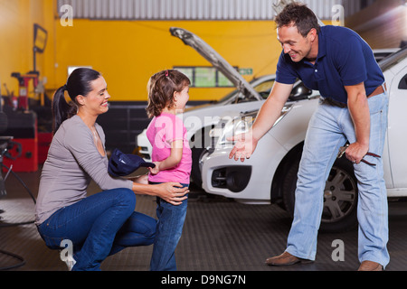 cute little girl hiding auto technician hat in garage Stock Photo