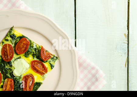 Spinach and tomato tart with feta cheese on a pink plate Stock Photo
