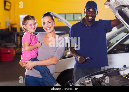 young mother and daughter in garage with auto mechanic Stock Photo