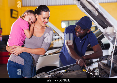 young mother taking her car for repair in garage with daughter sleeping on her shoulder Stock Photo