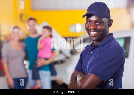 trustworthy African auto mechanic standing in front of family inside garage Stock Photo