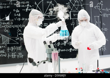 close-up of two people analyising substances in a chemistry lab with a blackboard with chemical formulas on the background Stock Photo