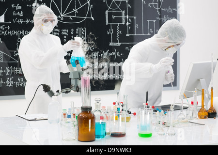 close-up of two scientists testing laboratory substances on a lab table with colorful liquids and transparent tools and a blackb Stock Photo