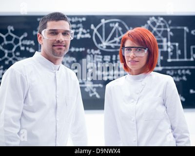 close-up of two researchers smiling in a chemistry lab with a blackboard on the background Stock Photo