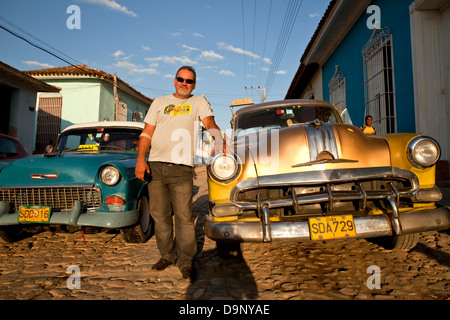 proud cuban man with his classic US car on a cobblestone street in the old town of Trinidad, Cuba, Caribbean Stock Photo