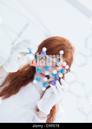 macro of a student in a chemistry lab holding in hands and analyzing DMT molecular model and a white board on the background Stock Photo