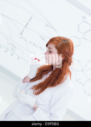 side-view of a pretty student in a chemistry lab smelling colorful substances and a white-board on the background Stock Photo