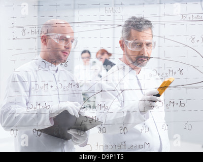 general-view of two scientists scaning and analyzig formulas on a transparent board with two students on the background Stock Photo