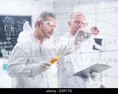 close-up of two scientists writing and analyzing graphics on a transparent board Stock Photo