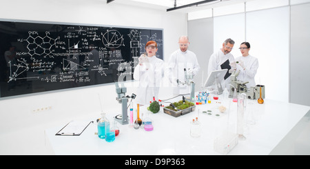 general-view of students in a chemistry lab conducting experiments under the supervision of two teachers and a blackboard with f Stock Photo
