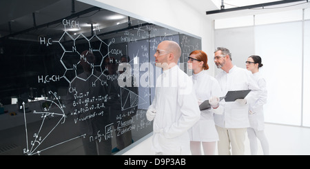 side-view of four scientists in a chemistry lab analyzing formulas on a blackboard Stock Photo
