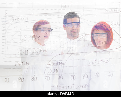close-up seen through a transparent board ot three scientists in a chemistry lab pointing and analyzing formulas on it Stock Photo