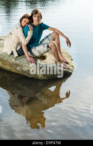 Couple sitting on rock by lake sharing romantic moment Stock Photo