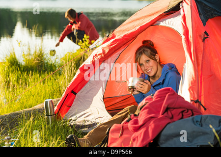 Camping girl sitting in tent drinking from pot Stock Photo