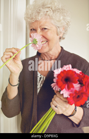 Cheerful senior lady smelling a flower indoors Stock Photo