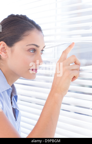 Brunette businesswoman peeking through a roller-blind Stock Photo