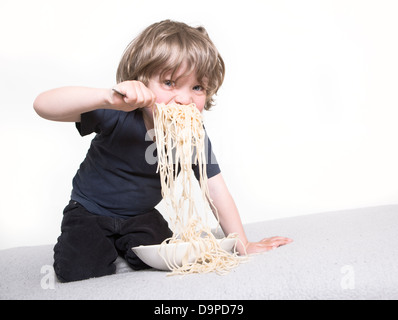 young boy eating his pasta on the couch Stock Photo