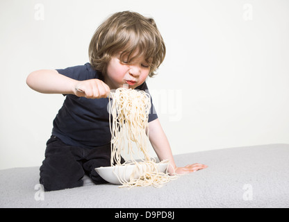 young boy eating his pasta on the couch Stock Photo