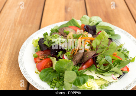 Salad with fried rabbit liver and fresh vegetables on a wooden table. Stock Photo