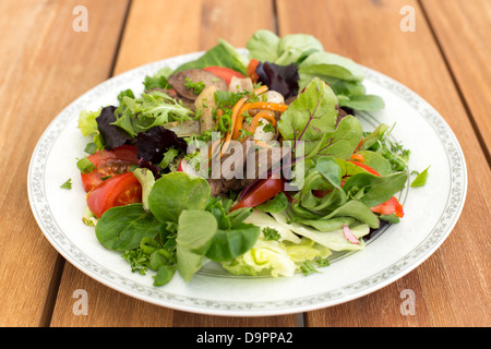 Mixed salad with fried rabbit liver and fresh vegetables on a wooden table. Stock Photo