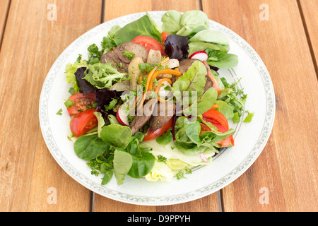 Salad with fried rabbit liver and fresh vegetables on a wooden table. Stock Photo