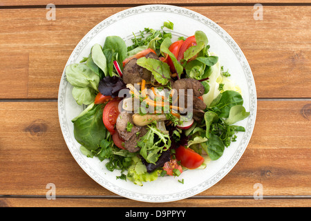 Summer salad with fried rabbit liver and fresh vegetables on a wooden table. Stock Photo