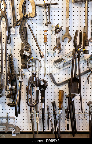 Assorted vintage tools and accessories hanging on a white pegboard. Stock Photo